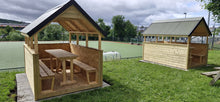 Two wooden shelters with tables and benches on a grassy area.