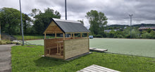 Wooden shed with a roof on a grassy area near a tennis court