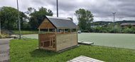 Wooden shed with a roof on a grassy area near a tennis court